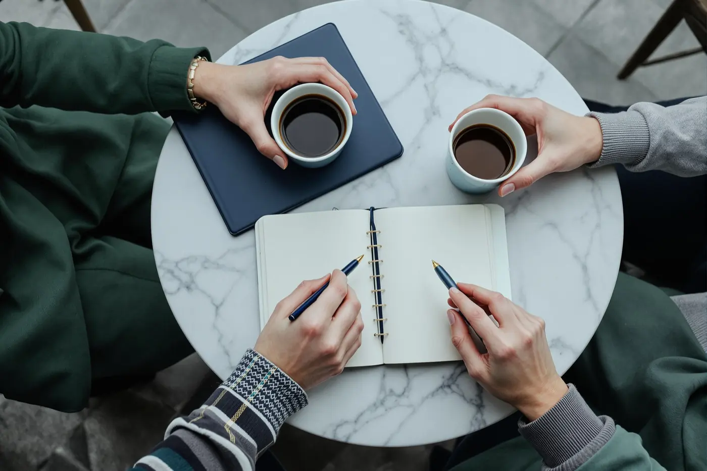 Two people talking over coffee with a notebook open on the table